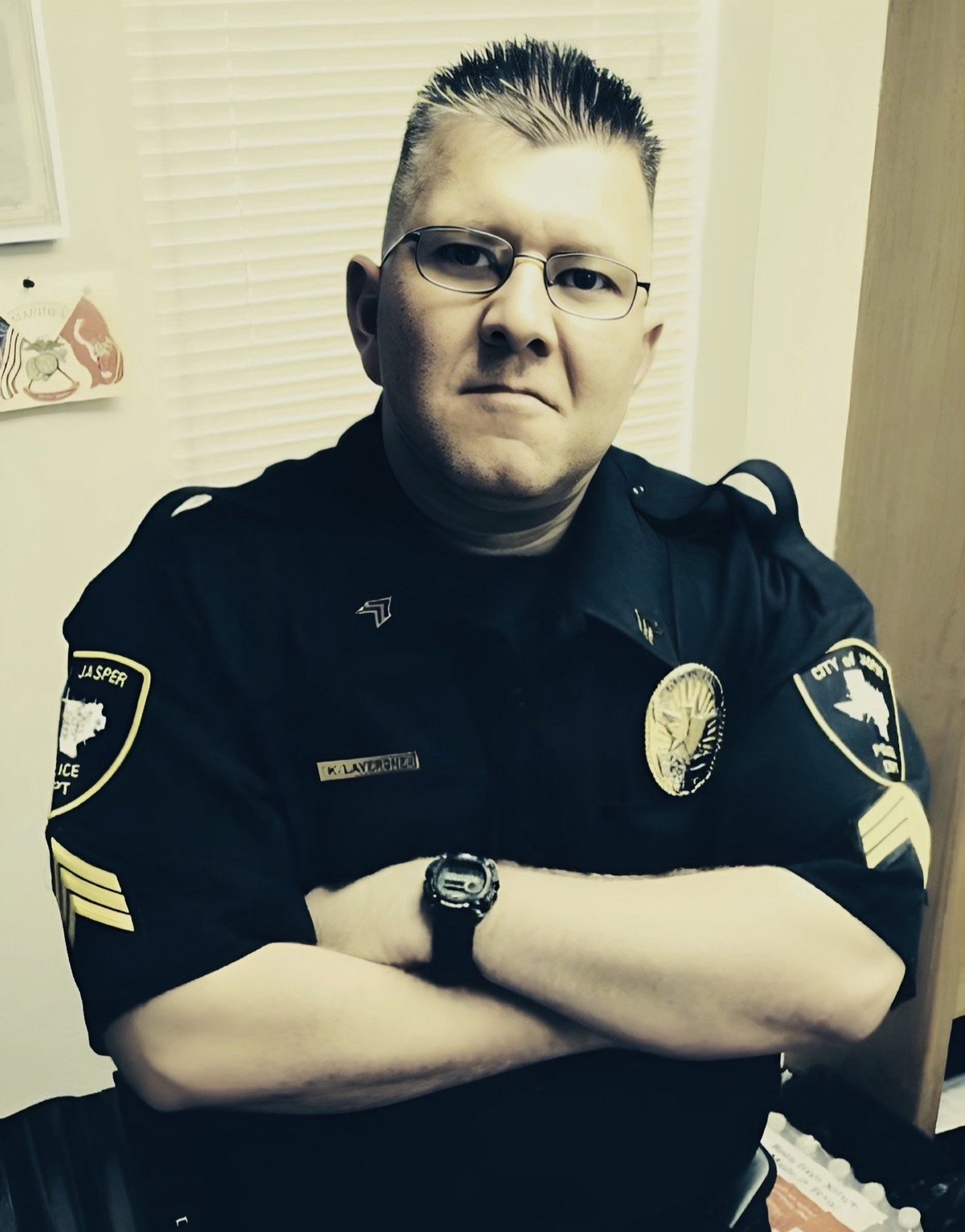Law enforcement officer in uniform with glasses and arms crossed, posed for official photograph indoors